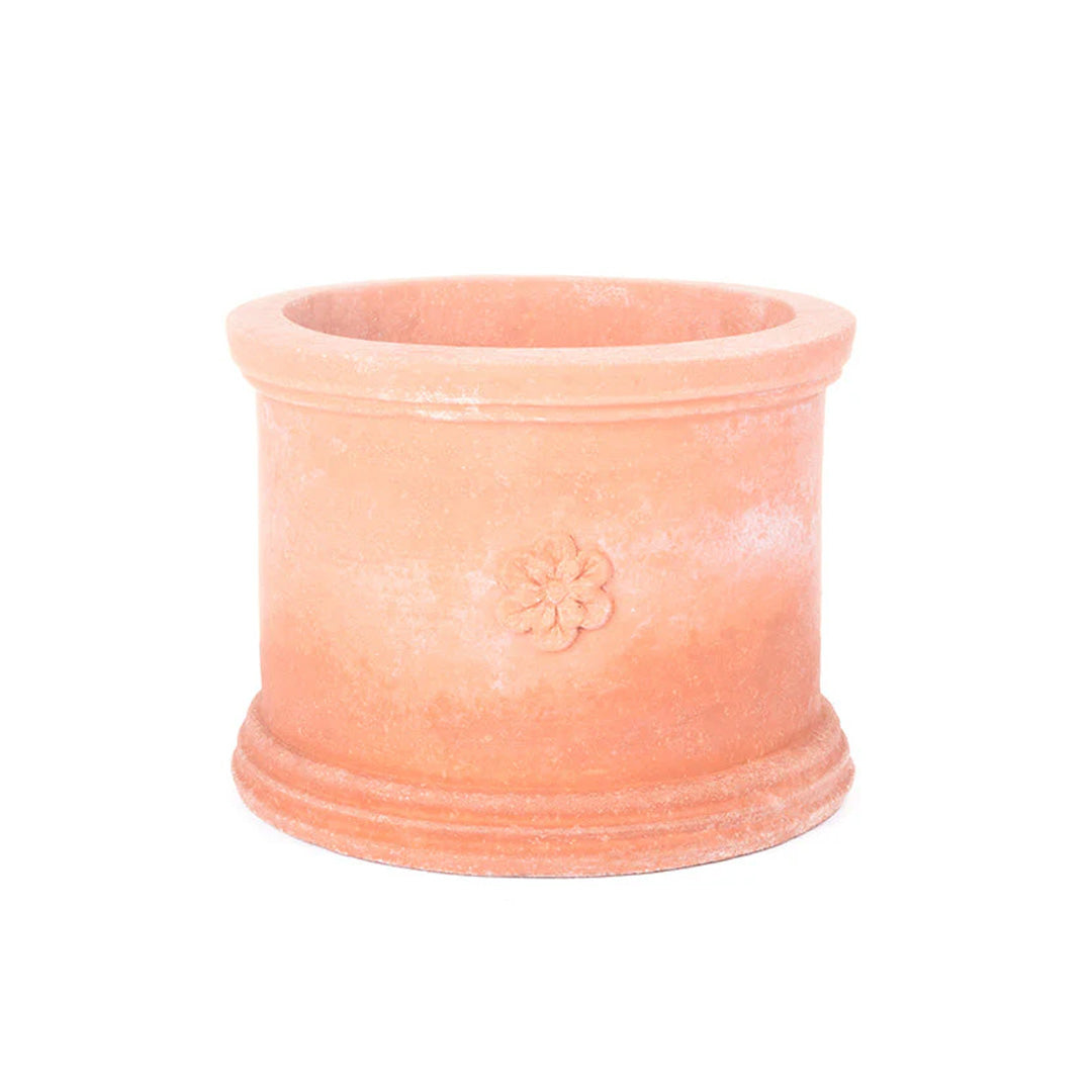 Lav, sylinderformet bruntonet terracottakrukke med bred kant og et lite blomsterornament på fremsiden.